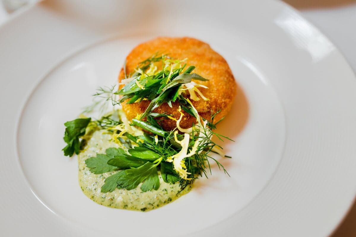 A golden Dungeness crab cake with herb salad and sauce gribiche