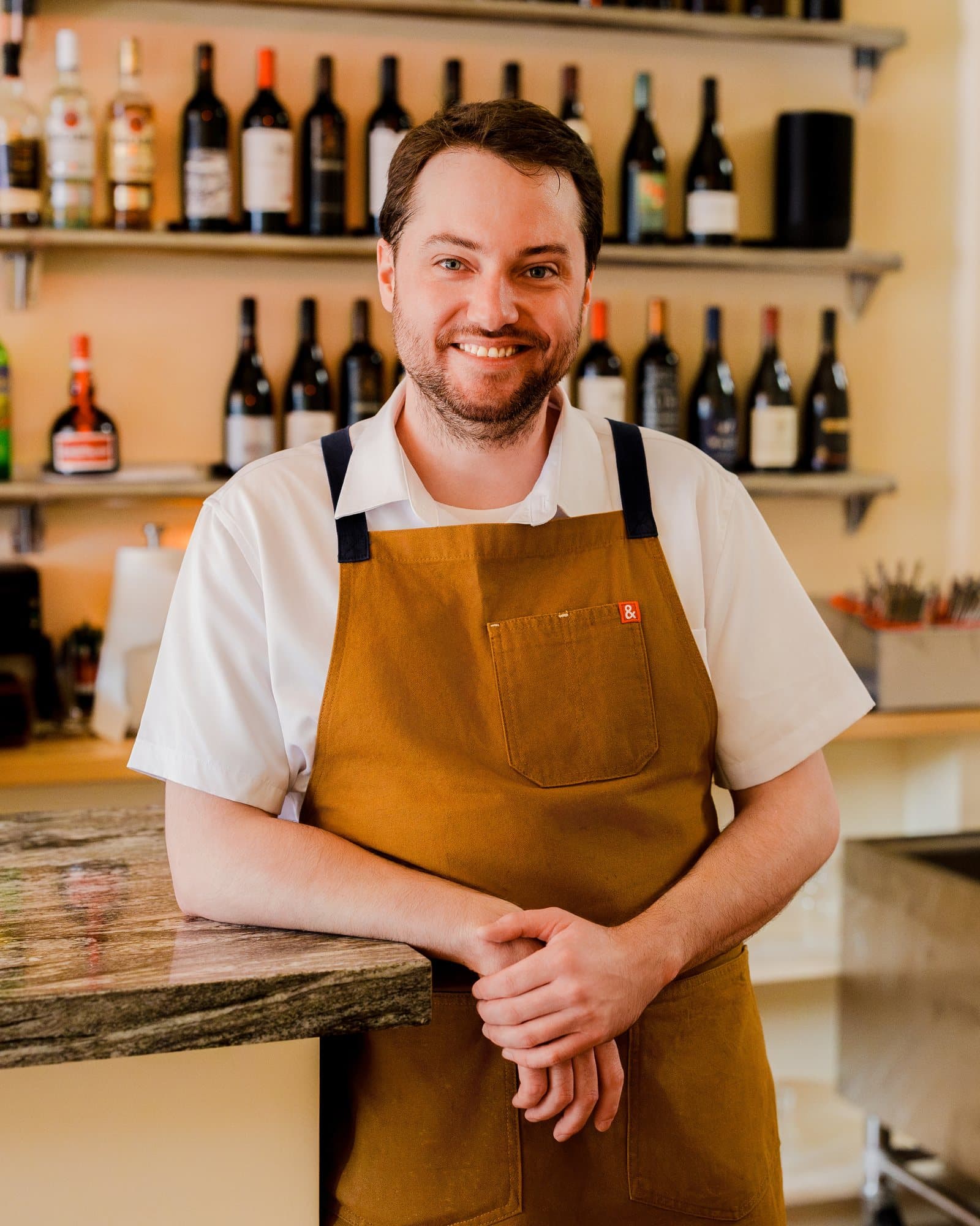 Dillon, bar manager, smiling in front of the wine shelves at the bar