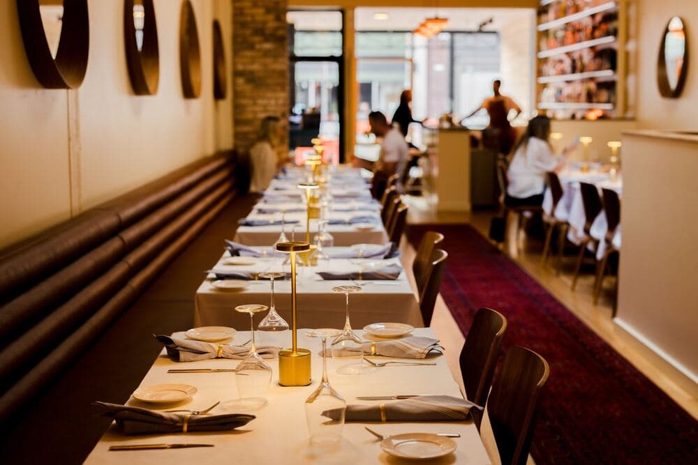 The dining room during dinner, with brass lamps along the banquette tables and guests out of focus beyond