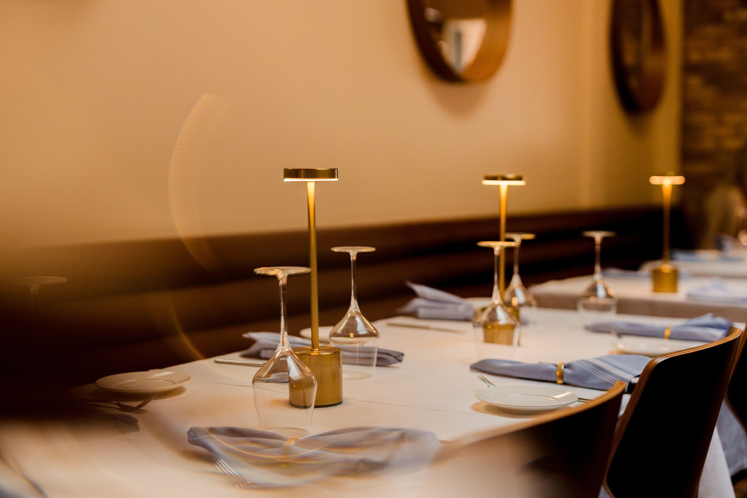 Brass lamps glowing along a row of set tables beside the banquette